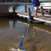 Person using the Beachroller lake weed removal tool with a 20ft handle and stainless steel blades.
